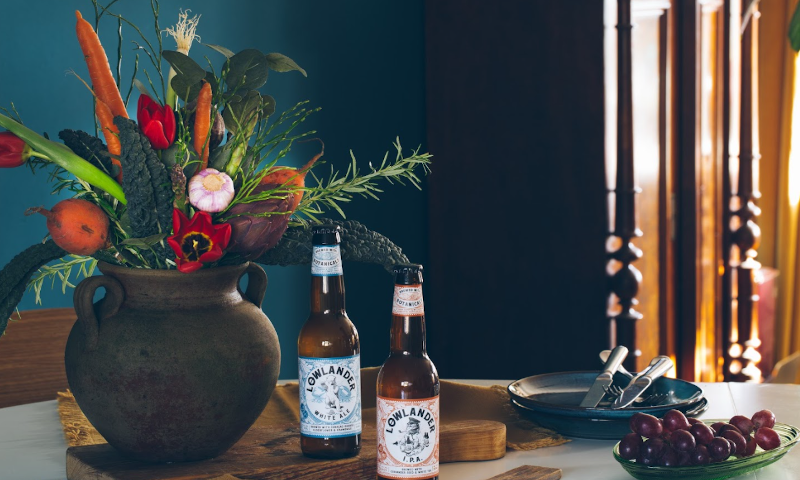 Lowlander boeket in een vaas met twee flesjes bier en gestapelde bordjes met bestek ernaast